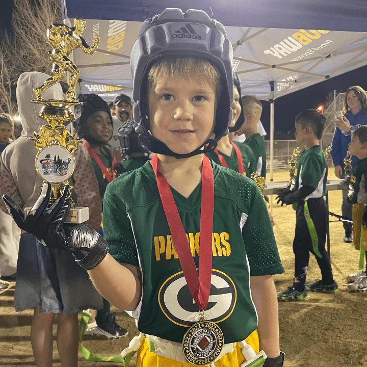 Child in Flag Football Uniform Holding Trophy